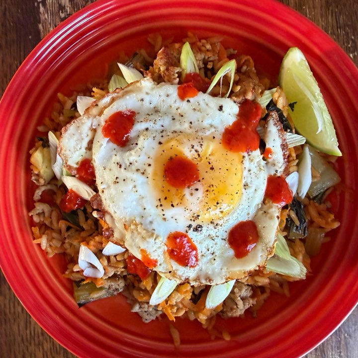 A Korean rice bowl with pork, vegetables and a fried egg with chilli sauce, on a red plate.