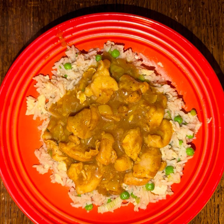 Chinese takeaway-style chicken curry on egg-fried rice with peas, on a red plate.