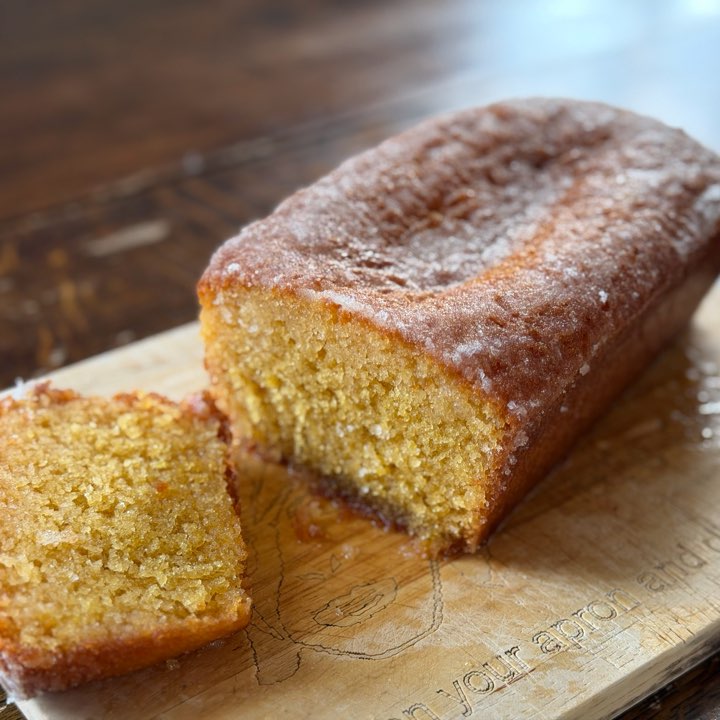 A lemon drizzle loaf with a slice cut, on a wooden board.