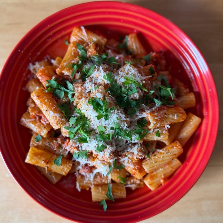 Rigatoni in a sausage ragu with parsley and grated Parmesan, on a red plate.